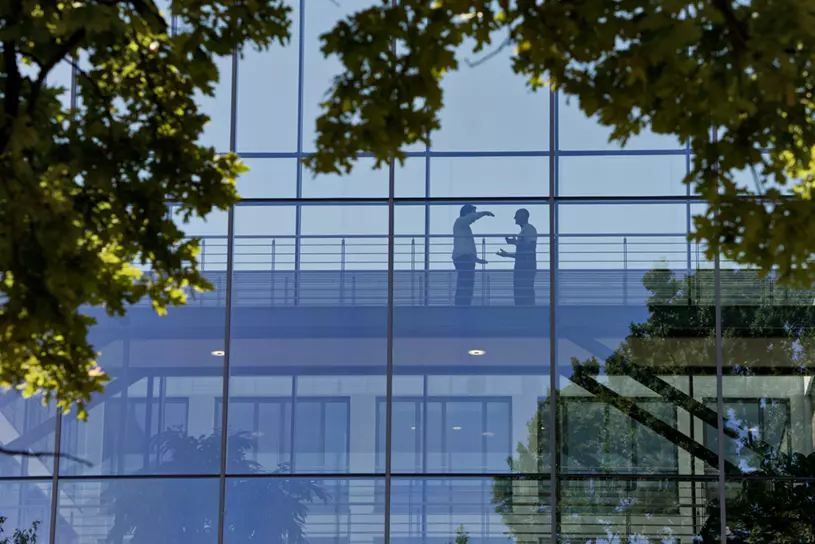 Zwei Personen unterhalten sich im Gebäude hinter einer Glasfassade